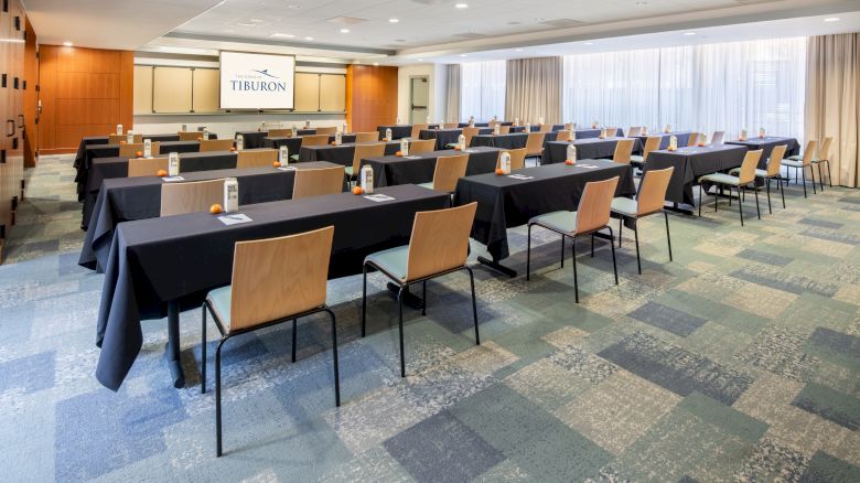 This image shows a conference room setup with rows of tables and chairs, black tablecloths, notepads, and a projector screen displaying 