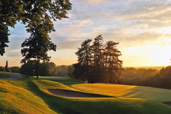 A serene golf course at sunset with lush green grass, sand bunkers, and tall trees, bathed in golden sunlight.