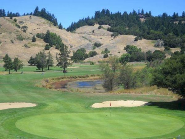 The image shows a green golf course with sand bunkers, a small pond, trees, and hills in the background ending the sentence.