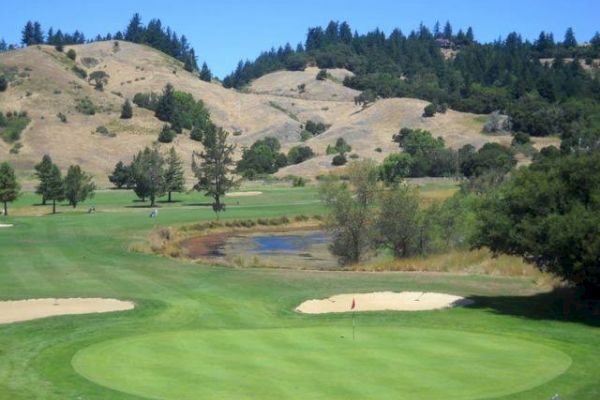 The image shows a green golf course with sand bunkers, a small pond, trees, and hills in the background ending the sentence.