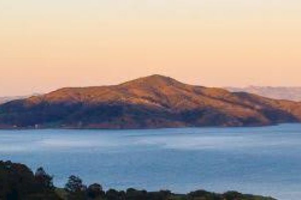 A serene landscape featuring an island surrounded by calm water, with a mountainous terrain under a clear sky during sunset.