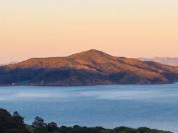 A serene landscape featuring an island surrounded by calm water, with a mountainous terrain under a clear sky during sunset.