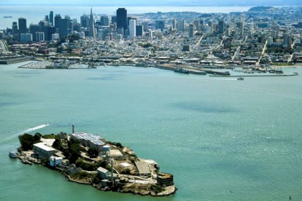 The image shows an aerial view of Alcatraz Island with San Francisco in the background, highlighting the cityscape and surrounding water.