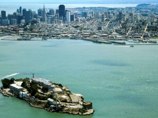 The image shows an aerial view of Alcatraz Island with San Francisco in the background, highlighting the cityscape and surrounding water.