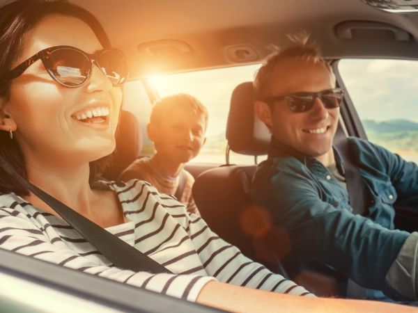 A family is enjoying a car ride with the sun shining; all are wearing sunglasses and seem content and happy while driving through a scenic route.