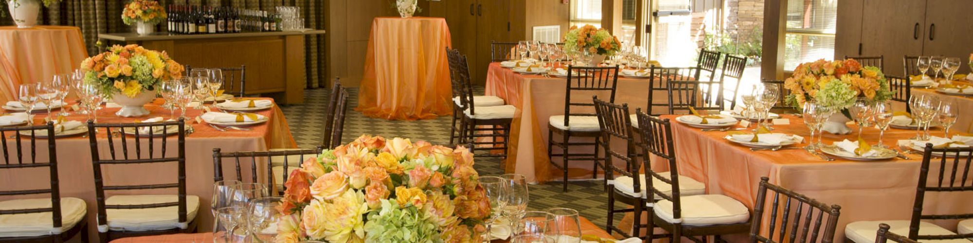 A beautifully decorated banquet hall with round tables set with orange tablecloths, elegant tableware, and flower centerpieces.