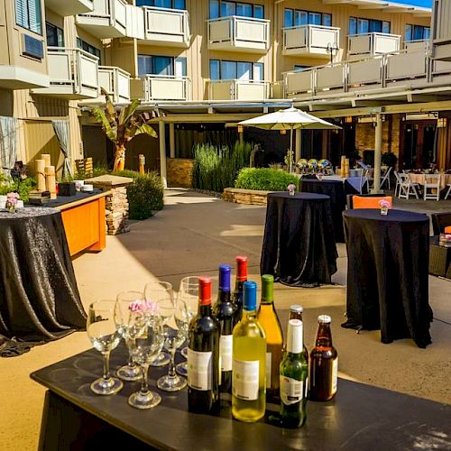 An outdoor event setup with tables, chairs, and a variety of drinks on a table, featuring a comfortable seating area and a modern building backdrop.