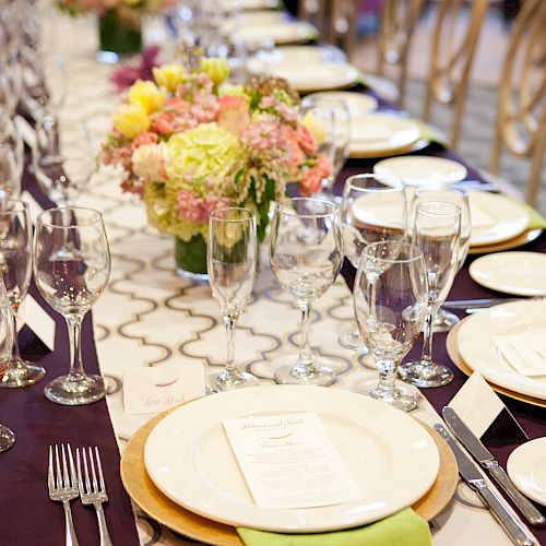 A long, elegantly set table with arranged flowers, white plates, and green napkins in a sophisticated, formal setting.