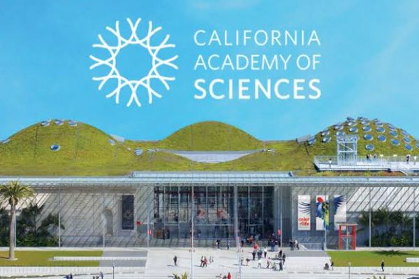 The image shows the entrance of the California Academy of Sciences, featuring a green roof, glass facade, and the institution's logo and name visible.