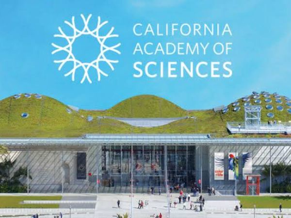 The image shows the entrance of the California Academy of Sciences, featuring a green roof, glass facade, and the institution's logo and name visible.