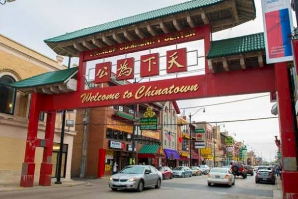 The image shows the entrance to a Chinatown neighborhood with a prominent "Welcome to Chinatown" sign and various shops and cars in the background.