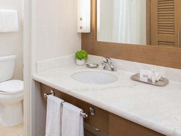 The image shows a modern bathroom with a toilet, a marble countertop sink, a large mirror, and various toiletries organized on the counter.