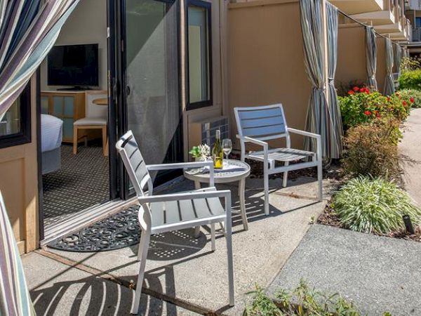 A small outdoor patio with two chairs and a table, with a bottle and glasses. It leads to an indoor living space with a TV and seating.