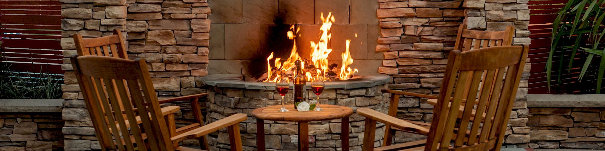 An outdoor fireplace with two wooden rocking chairs and a small table in between, creates a cozy setting.