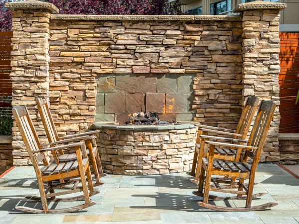 Four wooden rocking chairs surround an outdoor stone fireplace on a patio.