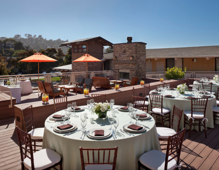 An outdoor patio setup with round tables prepared for dining, umbrellas, and a fireplace under a clear blue sky.
