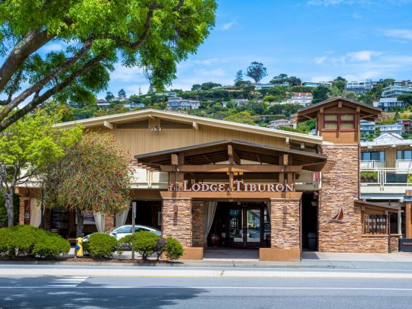 The Lodge at Tiburon hotel entrance with a stone facade, marquee sign, and leafy hillside buildings in the background.