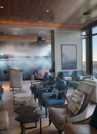 This image shows a modern lounge with comfortable seating, large windows offering a waterfront view, and a stylish wall mural of a cityscape.