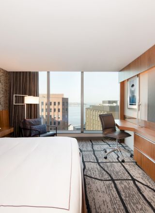 A modern hotel room with a large bed, flat-screen TV, desk, and a window offering a cityscape view.