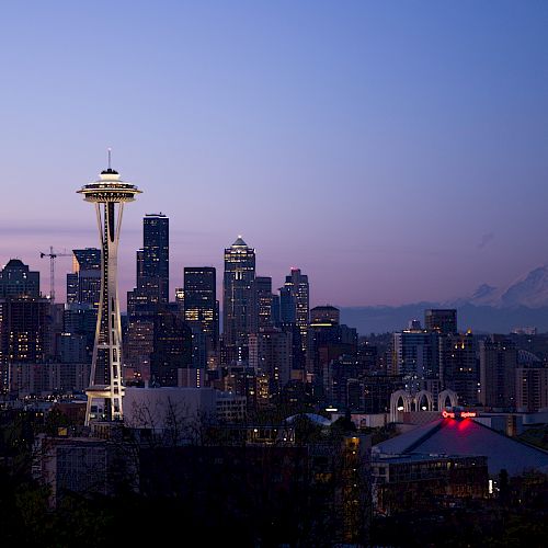 The image shows the Seattle skyline at twilight, featuring the Space Needle, various skyscrapers, and Mount Rainier in the background.