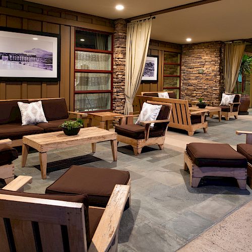 This image shows an outdoor seating area with wooden furniture, brown cushions, potted plants, and framed pictures on the walls.