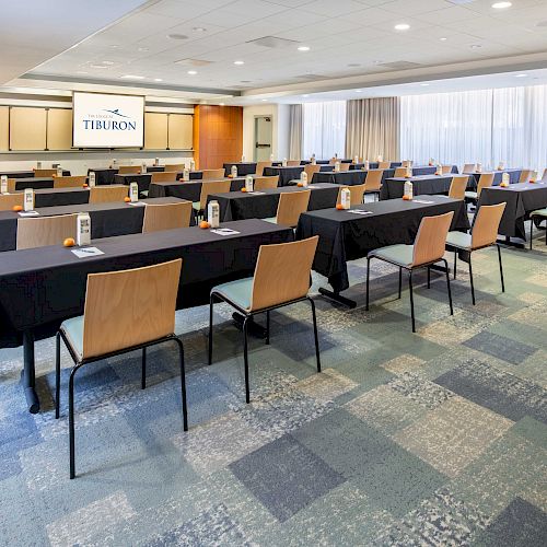 A conference room set up for a seminar with tables, chairs, table tents, notepads, and a large screen displaying 