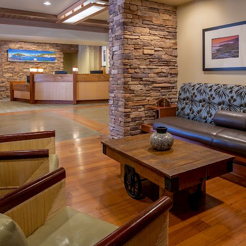 A cozy lobby area with comfortable seating, a wooden coffee table, artwork on the walls, and a reception desk in the background.