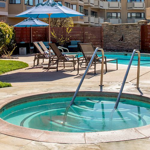 The image shows a serene outdoor area featuring a round jacuzzi and a swimming pool, with lounge chairs and umbrellas in the background.