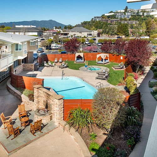 A residential area with a swimming pool, lounge chairs, an outdoor seating area, and surrounding buildings, with hills in the background.