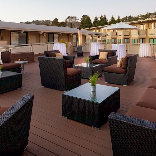 Outdoor lounge with wicker furniture, cushions, and tables arranged on a spacious deck. White umbrellas and cocktail tables add to the ambiance.