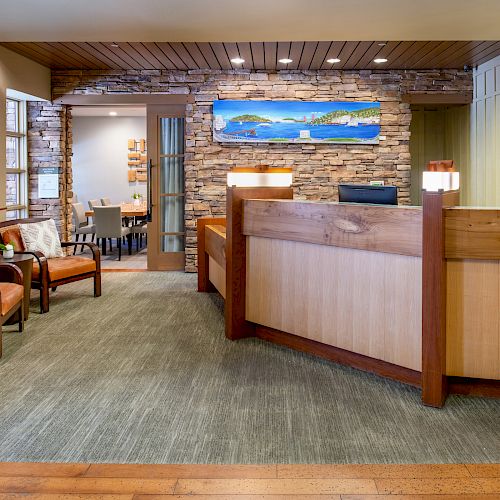 The image shows a modern reception area with a wooden desk, chairs, artworks, and a stone wall, leading to another room in the background.