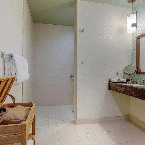 A modern bathroom with a wooden hamper, towels, a sink with a mirror, and pendant lights. The shower area has a tiled floor ending the sentence.