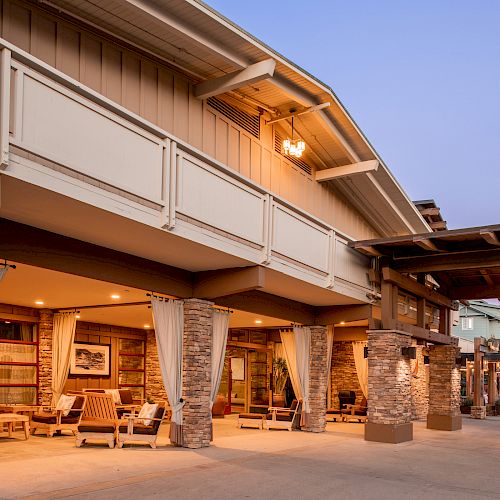 A welcoming exterior of a building with stone columns and draped curtains, featuring outdoor seating and warm lighting at twilight.